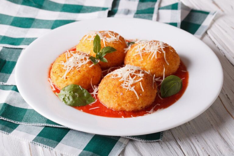 Arancini frits servis dans une assiette avec sauce tomate, basilic et fromage.