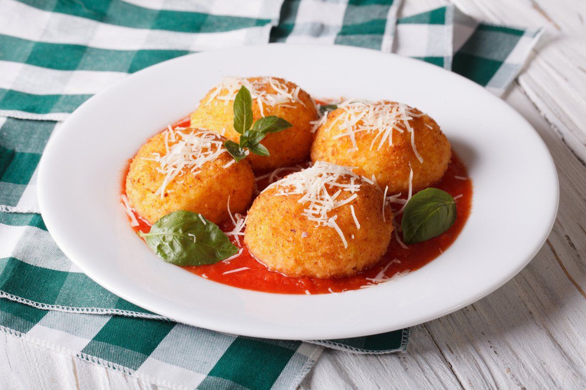 Arancini frits servis dans une assiette avec sauce tomate, basilic et fromage.