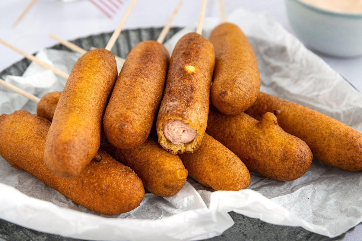 Plat de corn dogs dor&eacute;s et frits sur des b&acirc;tonnets, pr&ecirc;ts &agrave; &ecirc;tre d&eacute;gust&eacute;s.