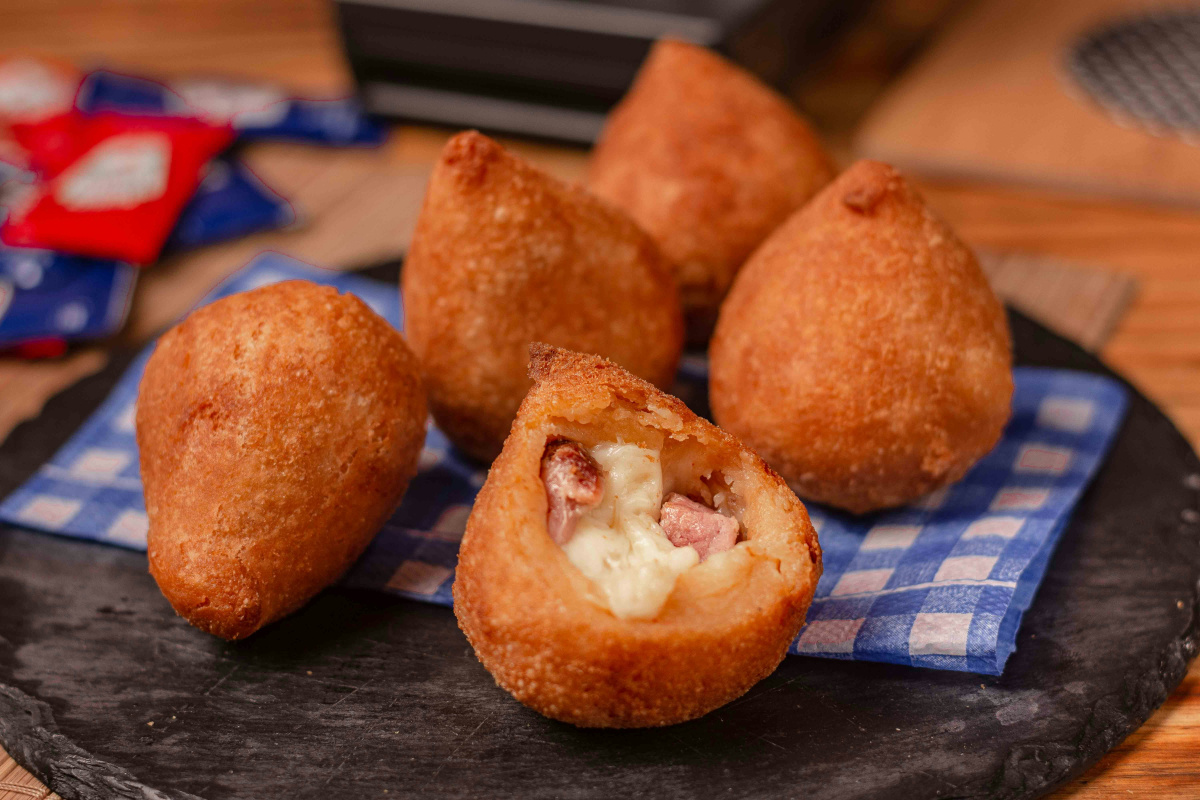 Coxinhas au jambon et fromage sur une ardoise, l'une ouverte.