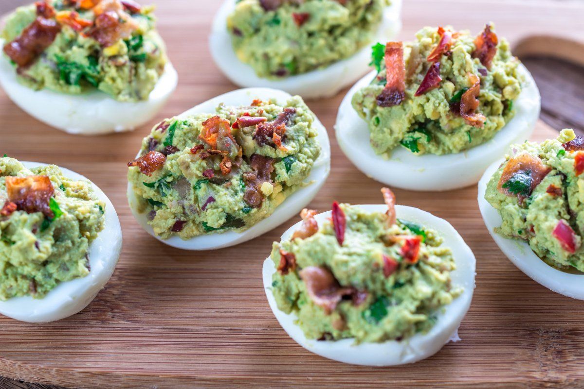 O&oelig;ufs mimosa au guacamole et bacon croustillant servis sur une planche en bois.