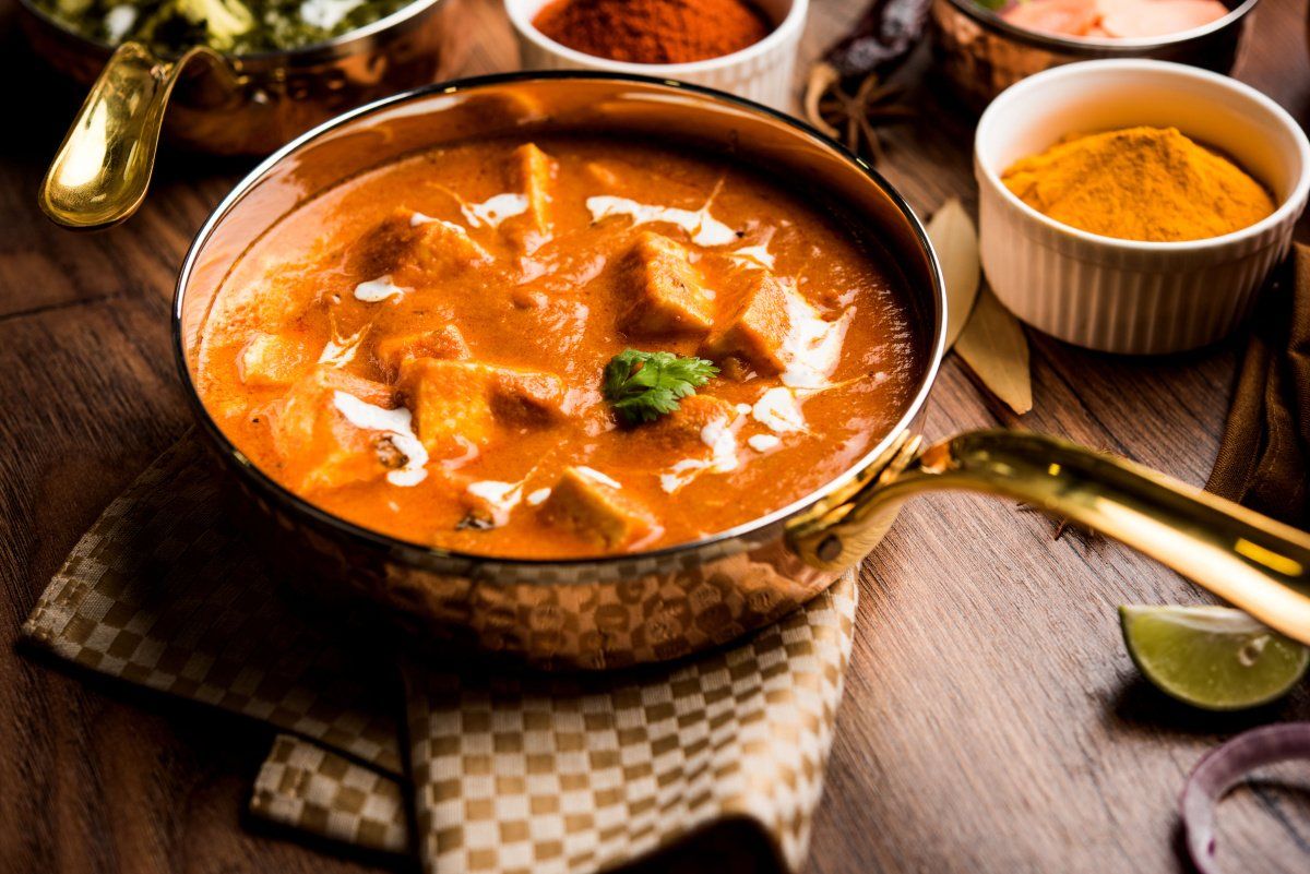 Paneer butter masala dans un bol en cuivre entour&eacute; d'&eacute;pices.