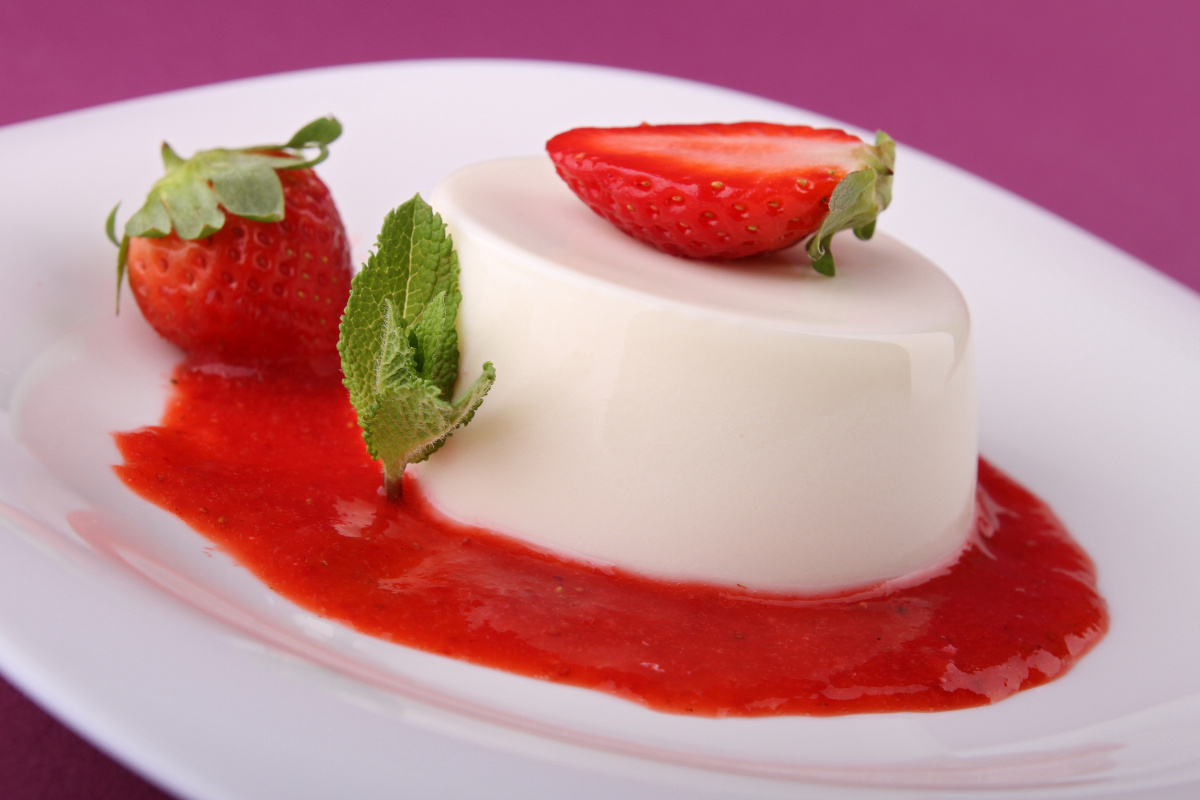 Panna cotta &agrave; la fraise servie avec coulis, fraises fra&icirc;ches et menthe.