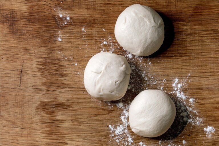 Pâtons de pâte à pizza maison sur une planche en bois farinée.