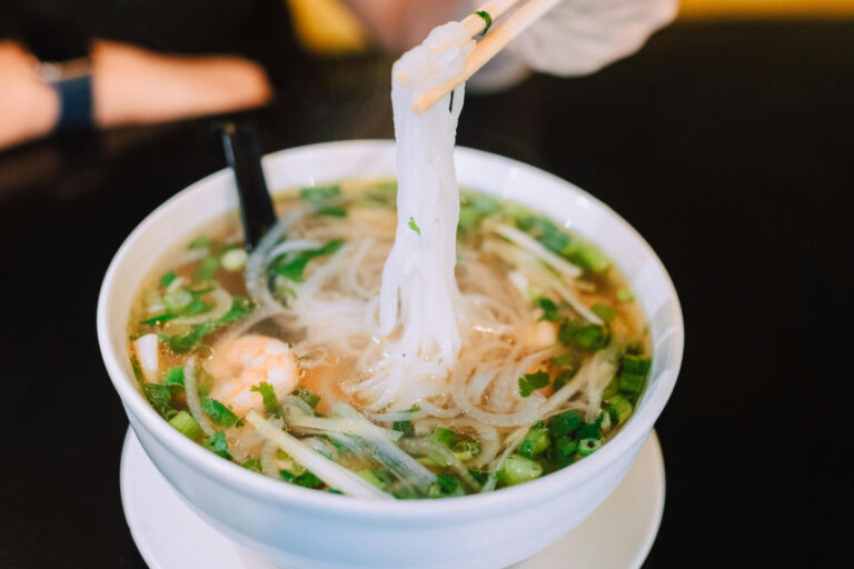 Bol de soupe phở vietnamienne fumante aux crevettes et herbes fraîches.