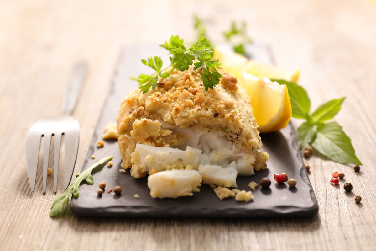 Filet de poisson en cro&ucirc;te de noisettes servi avec du citron.