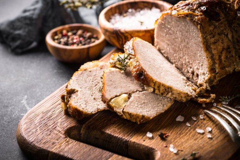 Rôti de porc aux herbes tranché sur une planche avec sel et poivre.