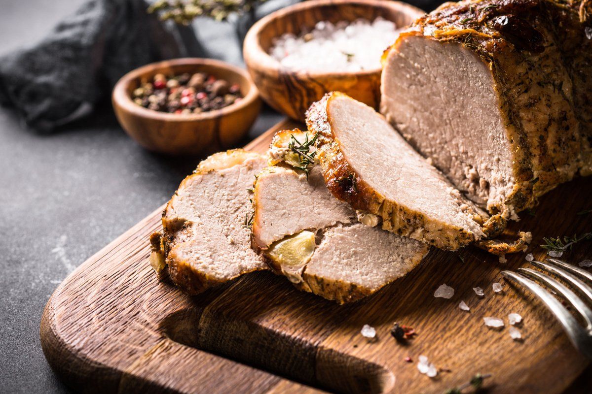 R&ocirc;ti de porc aux herbes tranch&eacute; sur une planche avec sel et poivre.