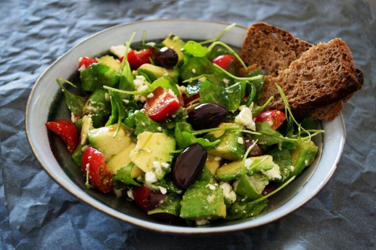 Bol de salade fraîche avec avocat, tomates cerises, feta, olives et pain complet.