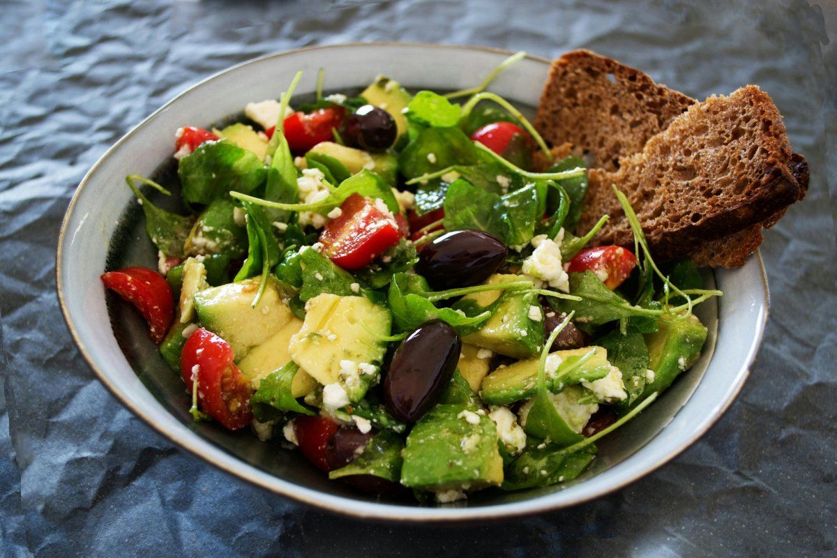 Bol de salade fra&icirc;che avec avocat, tomates cerises, feta, olives et pain complet.