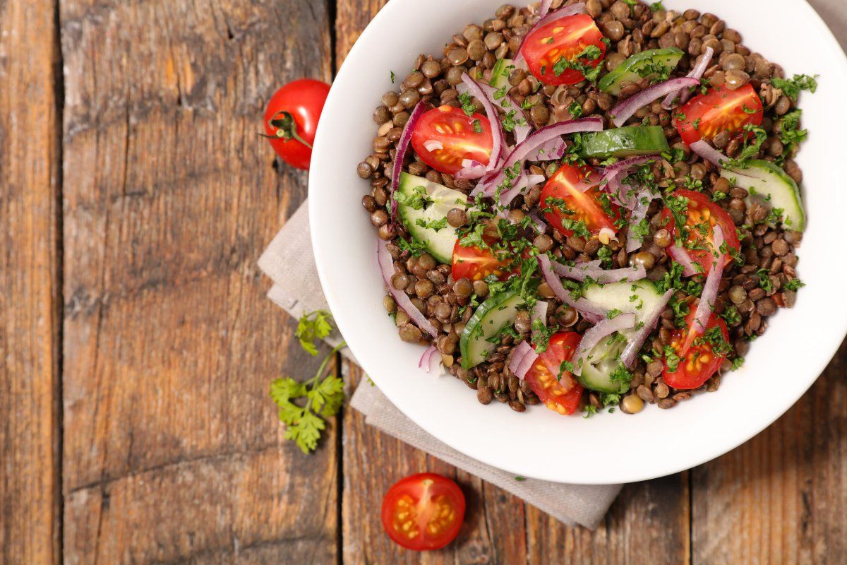 Bol blanc de salade de lentilles, tomates, concombre et oignon sur une table en bois.