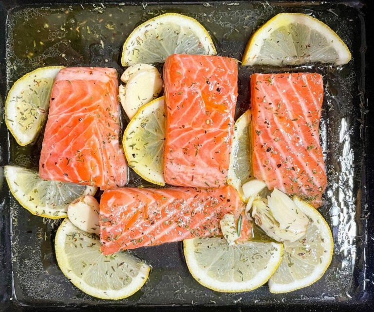 Pavés de saumon cru sur une plaque de cuisson avec citron, ail et herbes.