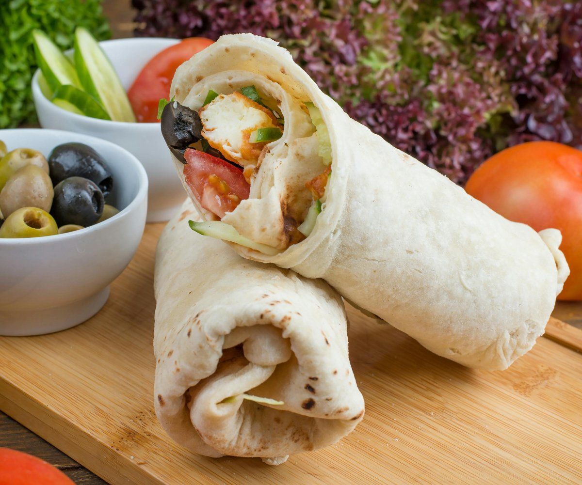 Deux wraps au poulet sur une planche en bois avec des olives et crudit&eacute;s.