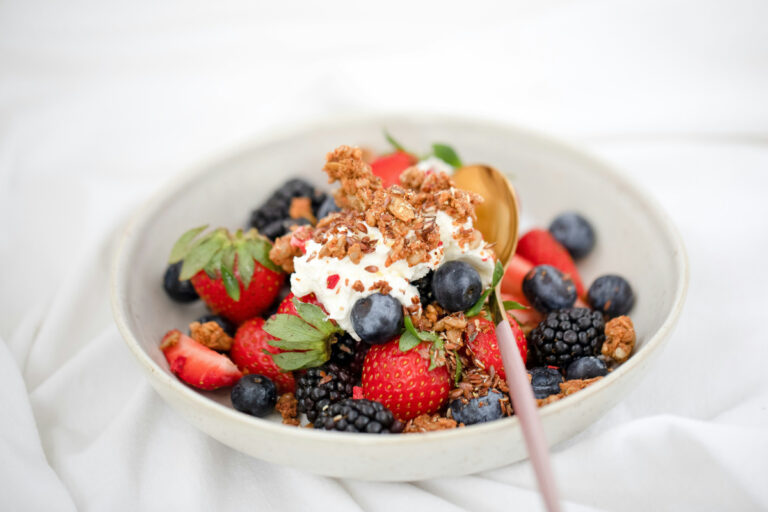 Bol de yaourt et granola garni de fraises, myrtilles et mûres fraîches.