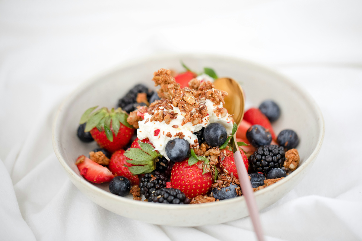 Bol de yaourt et granola garni de fraises, myrtilles et m&ucirc;res fra&icirc;ches.
