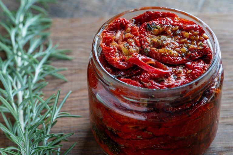 Bocal en verre de tomates séchées marinées à l'huile, ail et romarin frais.