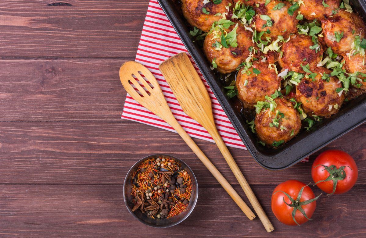Plat de boulettes de viande sortant du four, d&eacute;cor&eacute; avec du basilic hach&eacute;.