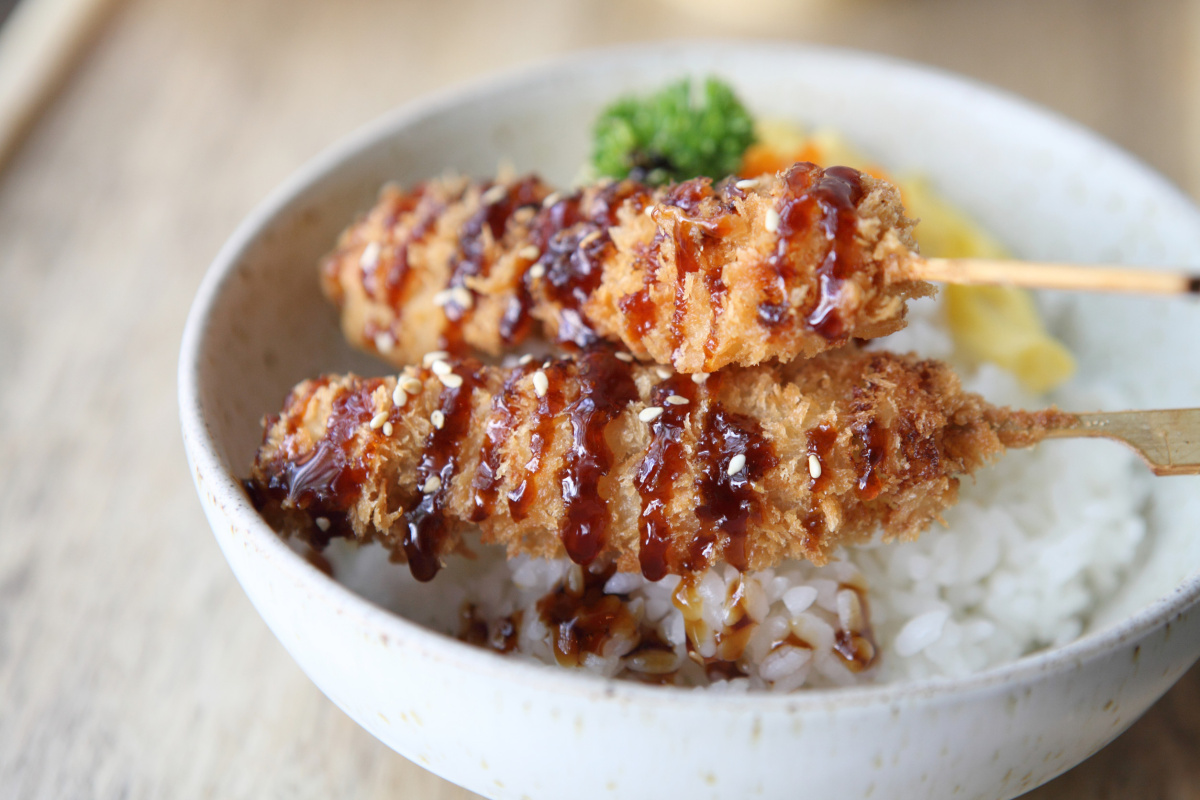 Bol de riz blanc surmont&eacute; de brochettes de porc pan&eacute; tonkatsu avec sauce.