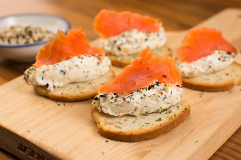Canapés au saumon fumé et fromage frais aux herbes servis sur une planche.