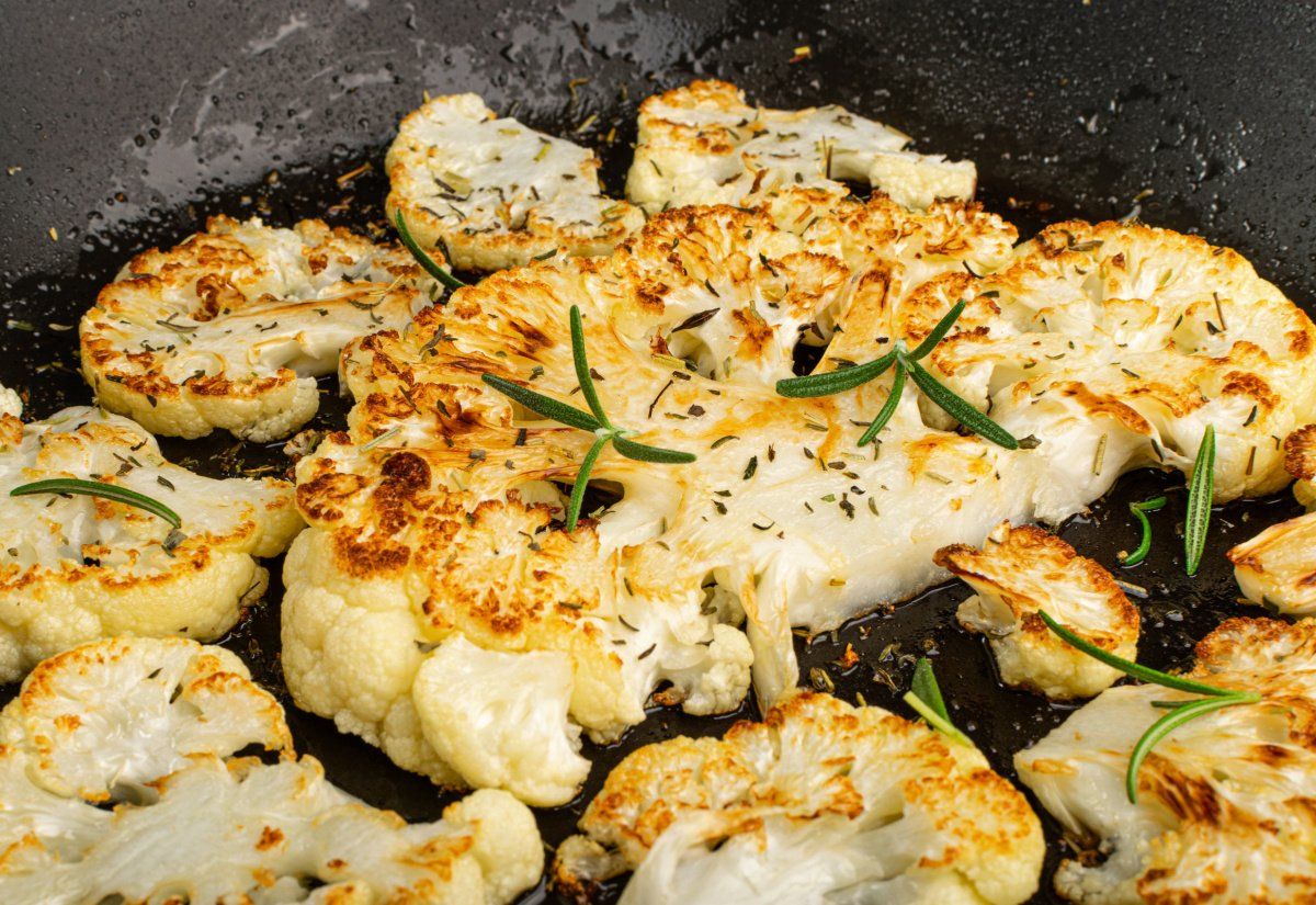 Tranches de chou-fleur dor&eacute;s cuisant dans une po&ecirc;le avec du romarin.