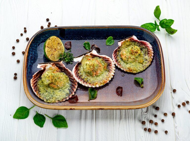 Coquilles Saint-Jacques gratinées au pesto servies avec du citron vert.