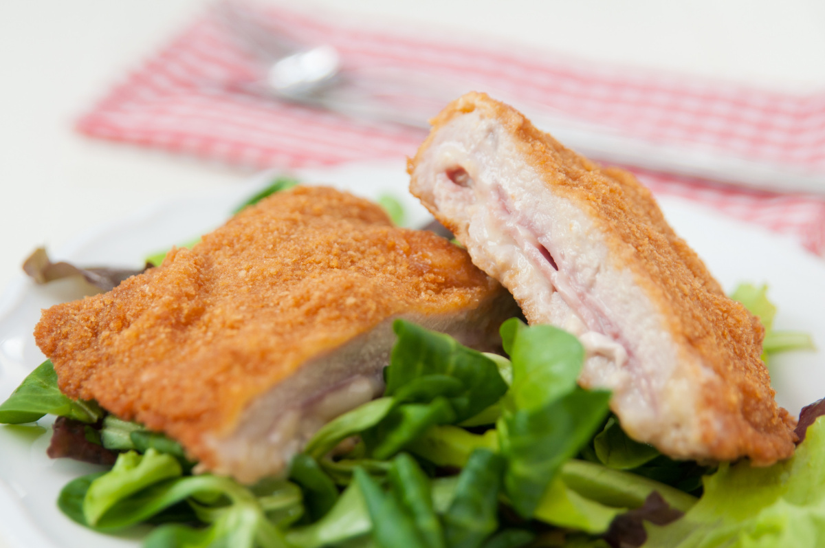 Cordon bleu pan&eacute; et coup&eacute; en deux, servi sur un lit de salade verte.
