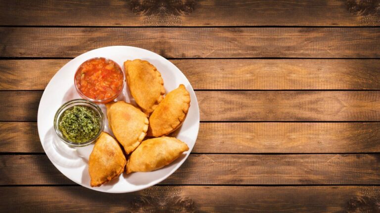 Assiette d'empanadas argentins dorés avec sauces sur une table en bois rustique.
