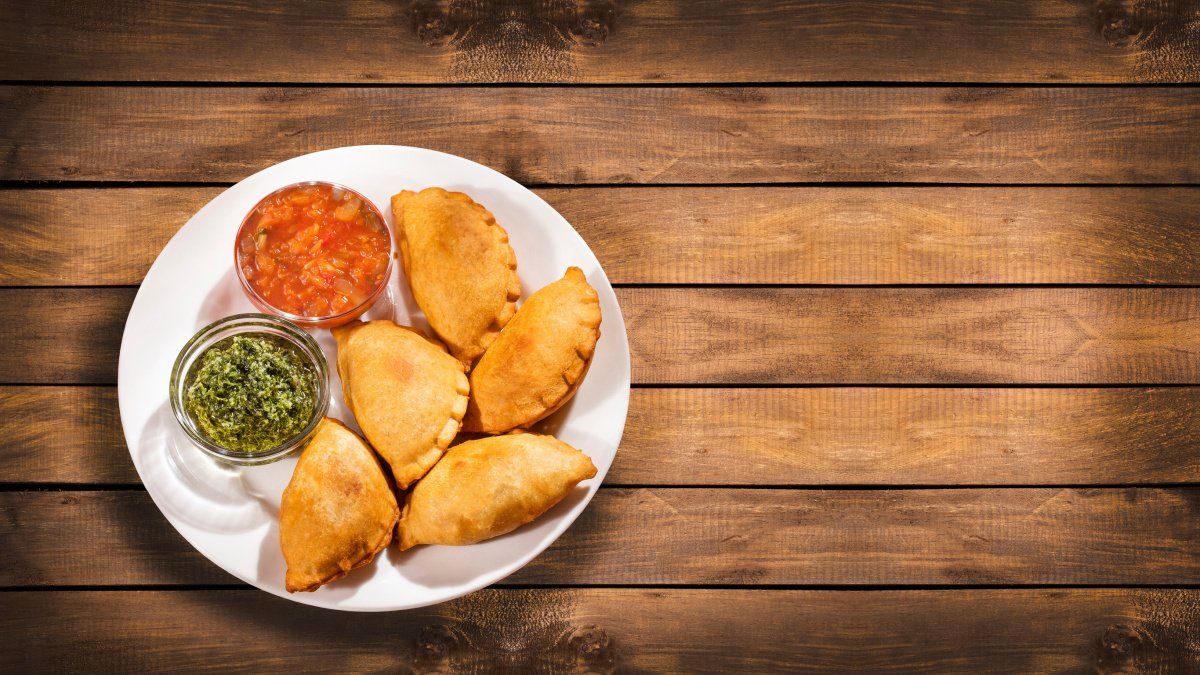 Assiette d'empanadas argentins dor&eacute;s avec sauces sur une table en bois rustique.