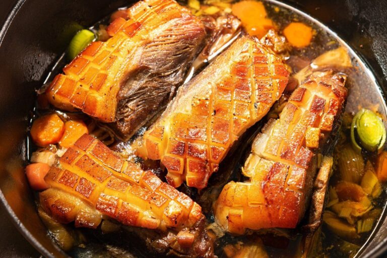 Morceaux d'epaule de porc à la peau croustillante mijotant avec des légumes en cocotte.