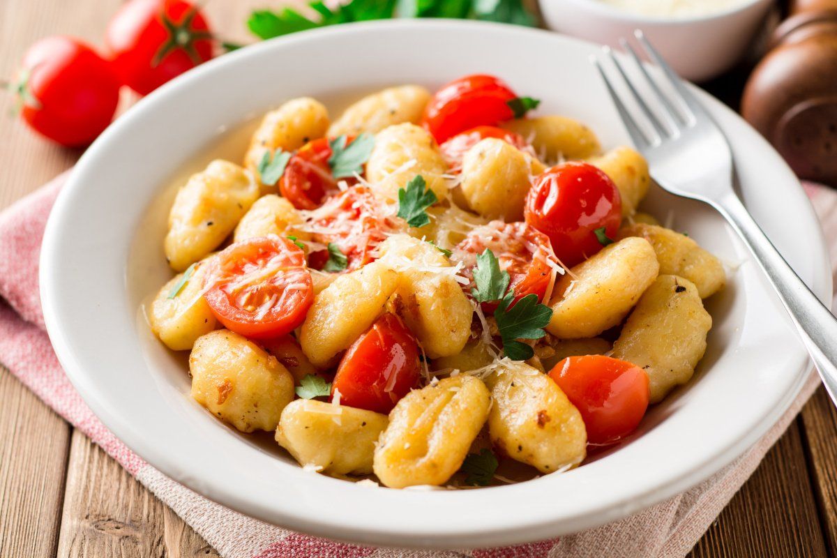 Assiette blanche de gnocchis po&ecirc;l&eacute;s aux tomates cerises, persil et parmesan r&acirc;p&eacute;.