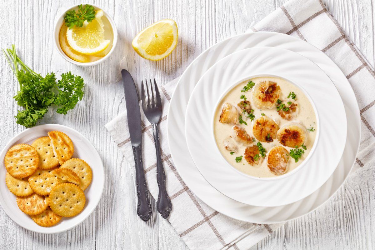 Plat de noix de Saint-Jacques po&ecirc;l&eacute;es dans une sauce cr&egrave;me, servi avec du persil.
