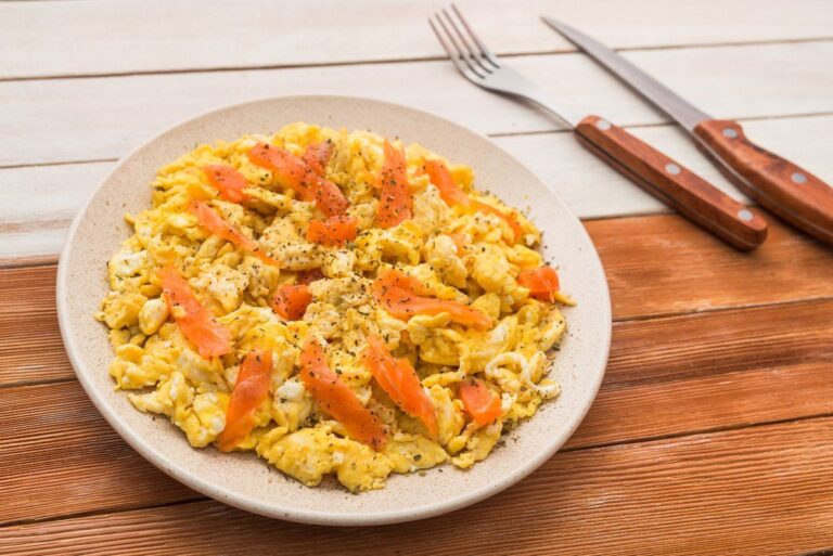 Assiette d'œufs brouillés crémeux au saumon fumé, servis sur une table en bois.