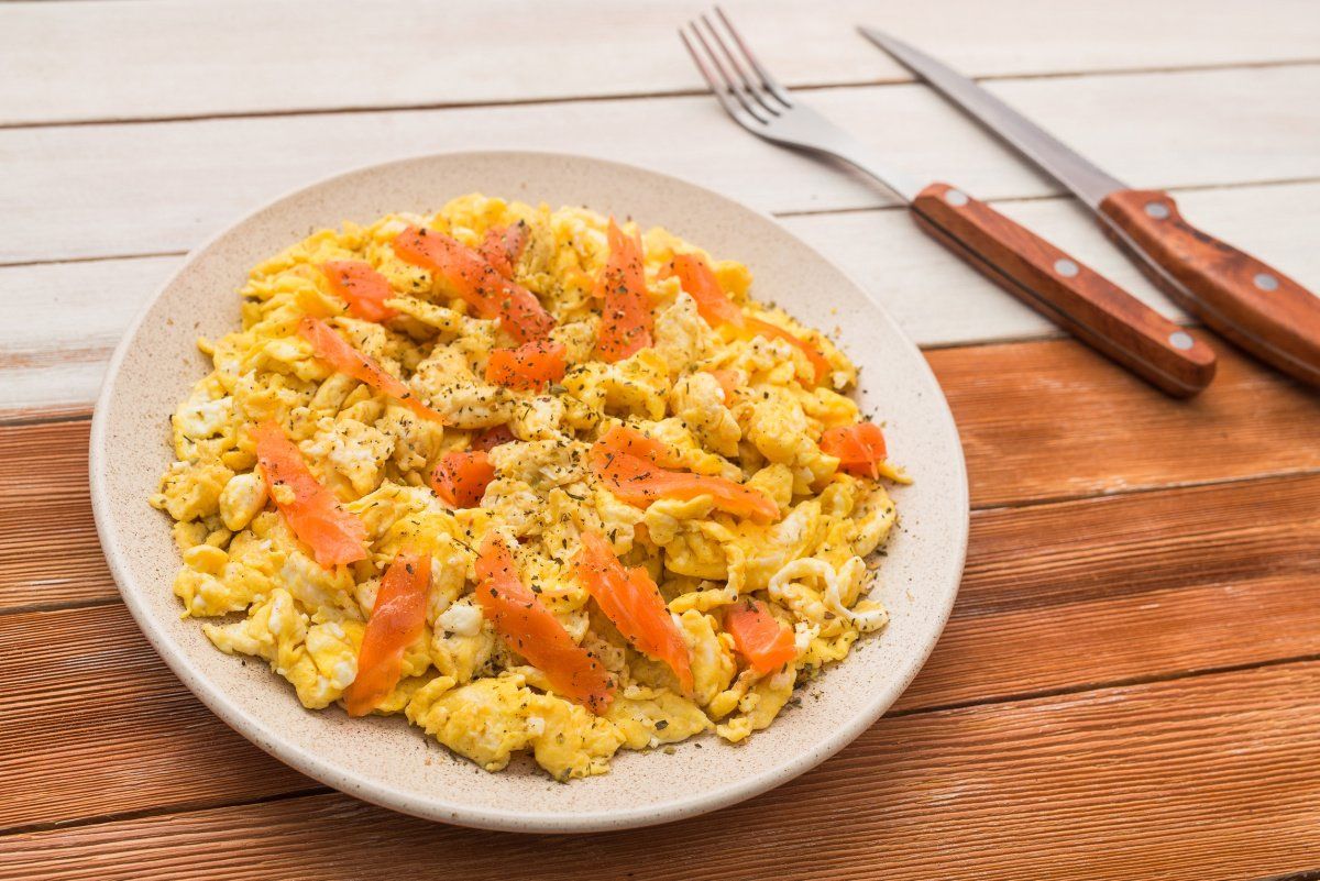 Assiette d'&oelig;ufs brouill&eacute;s cr&eacute;meux au saumon fum&eacute;, servis sur une table en bois.