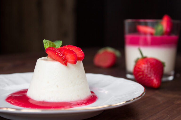 Panna cotta démoulée avec coulis, fraises fraîches et menthe.