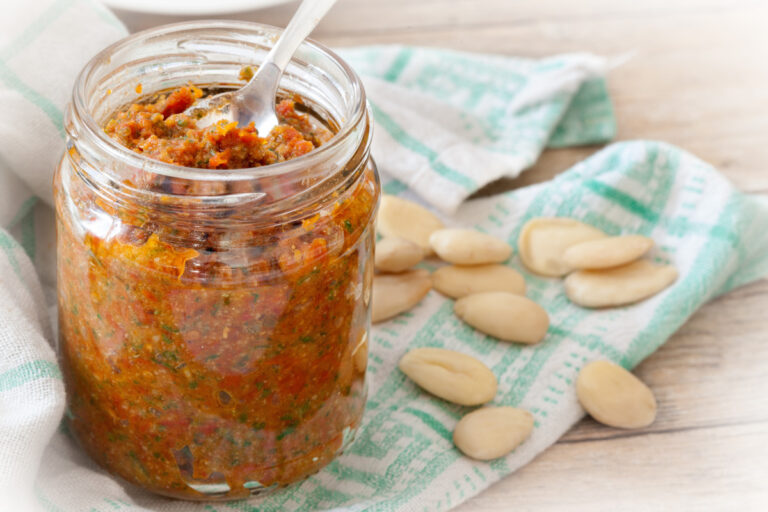 Bocal en verre de pesto de tomates maison avec des amandes sur une table.