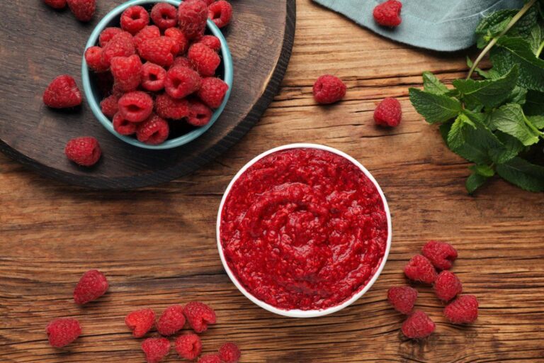 Purée de framboises dans un bol avec des fruits frais autour.