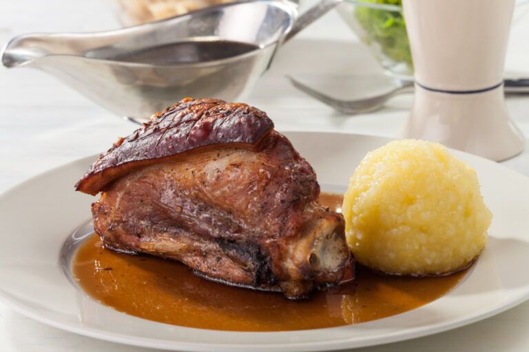 Jarret de porc rôti bavarois servi avec une boulette de pomme de terre et sa sauce.