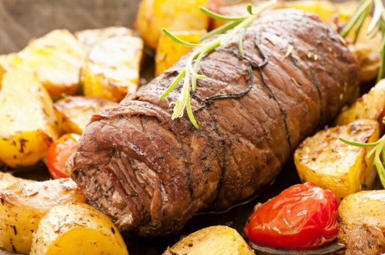 Roulade de bœuf rôtie garnie de romarin avec pommes de terre et tomates roties.