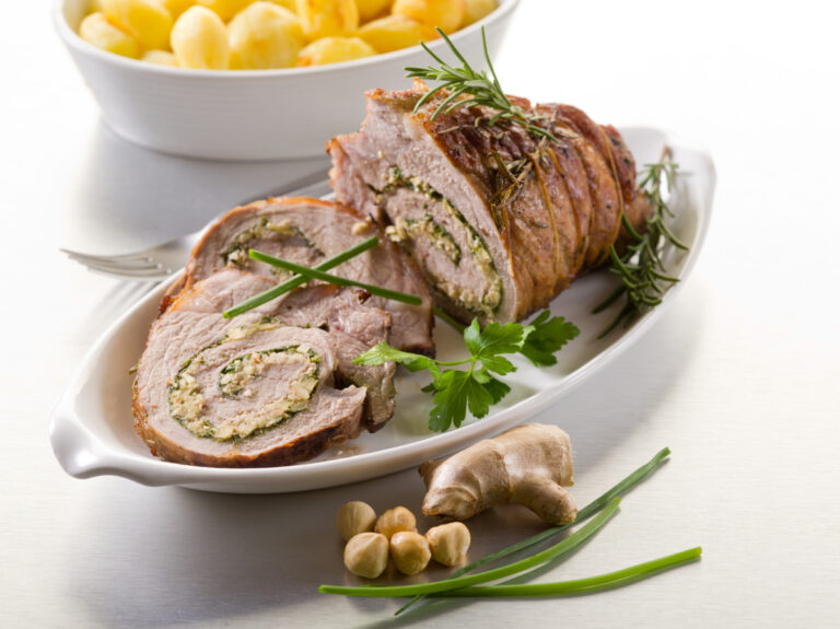 Roulé de veau farci et tranché servi dans un plat avec des pommes de terre.