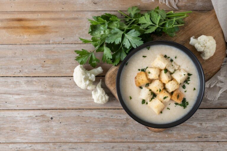 Bol de soupe de chou-fleur avec croûtons et persil, vue de dessus sur table en bois.