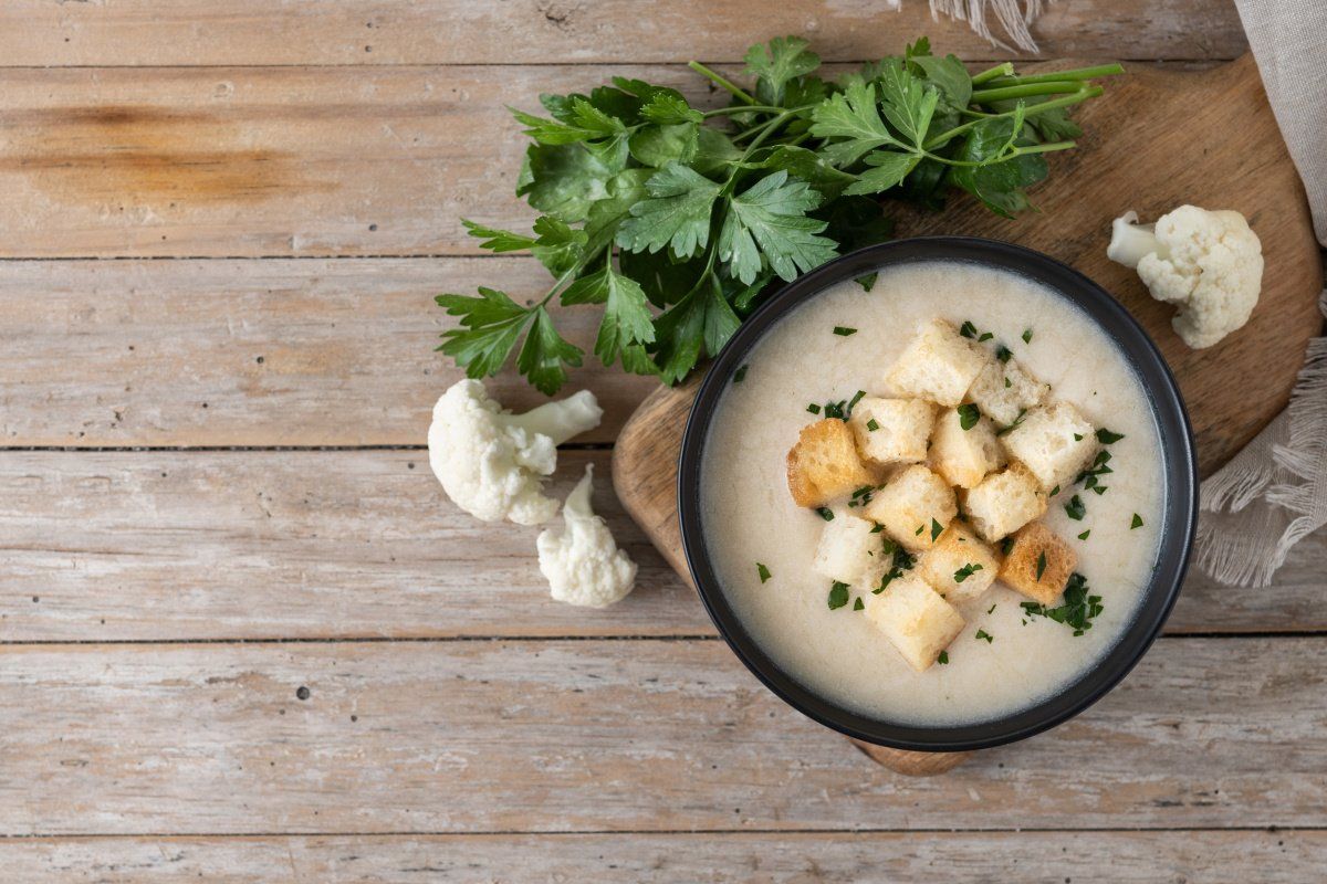 Bol de soupe de chou-fleur avec cro&ucirc;tons et persil, vue de dessus sur table en bois.