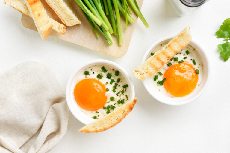 Ramequins d'œufs cocotte garnis de ciboulette, servis avec des mouillettes grillées.