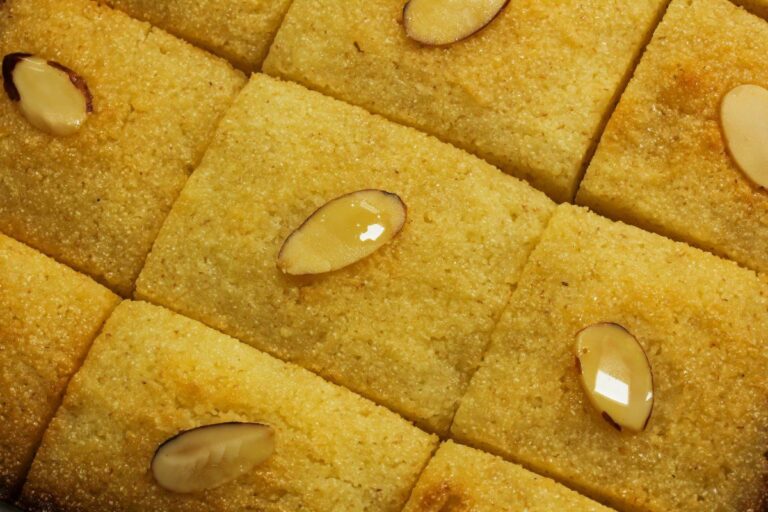 Gâteau de semoule basbousa doré, découpé en losanges et garni d'amandes effilées.