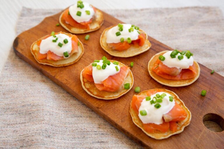 Amuse-bouches de blinis au saumon fumé et crème, parsemés de ciboulette.