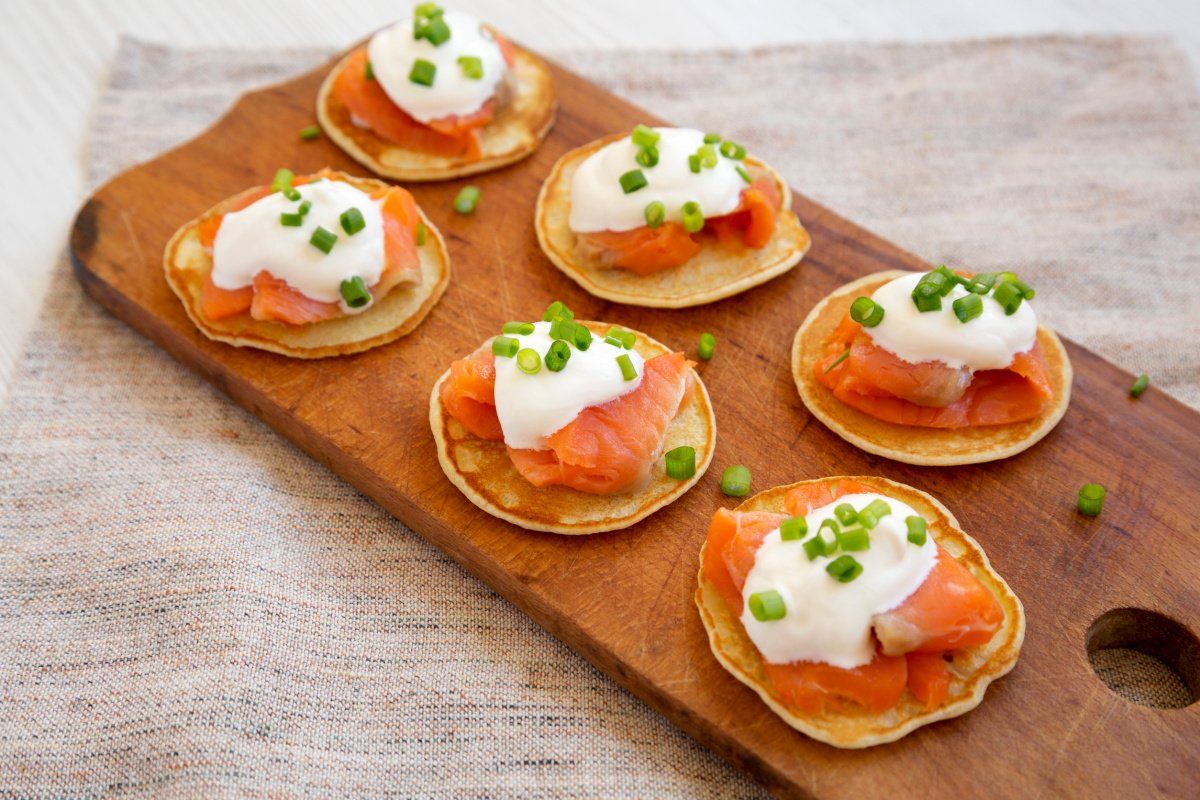 Amuse-bouches de blinis au saumon fum&eacute; et cr&egrave;me, parsem&eacute;s de ciboulette.
