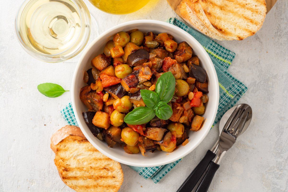 Caponata sicilienne aux aubergines, olives, tomates et basilic frais dans un bol.