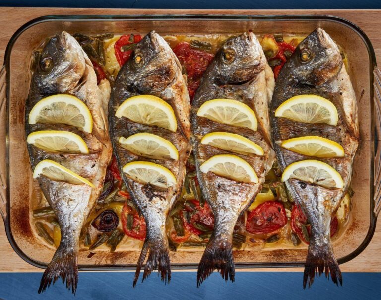 Plat de daurades entières au citron au four sur un lit de légumes.