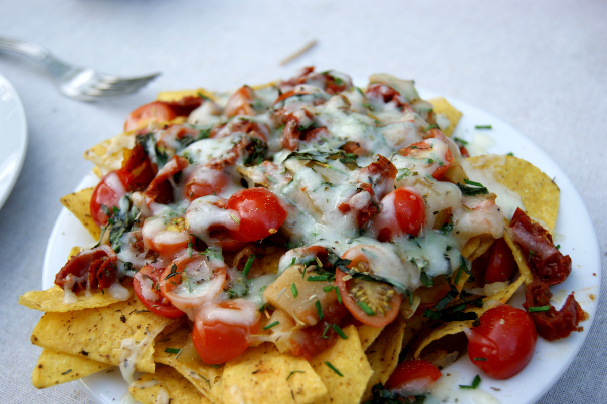 Nachos gratin&eacute;s au fromage, garnis de tomates cerises et d'herbes fra&icirc;ches.