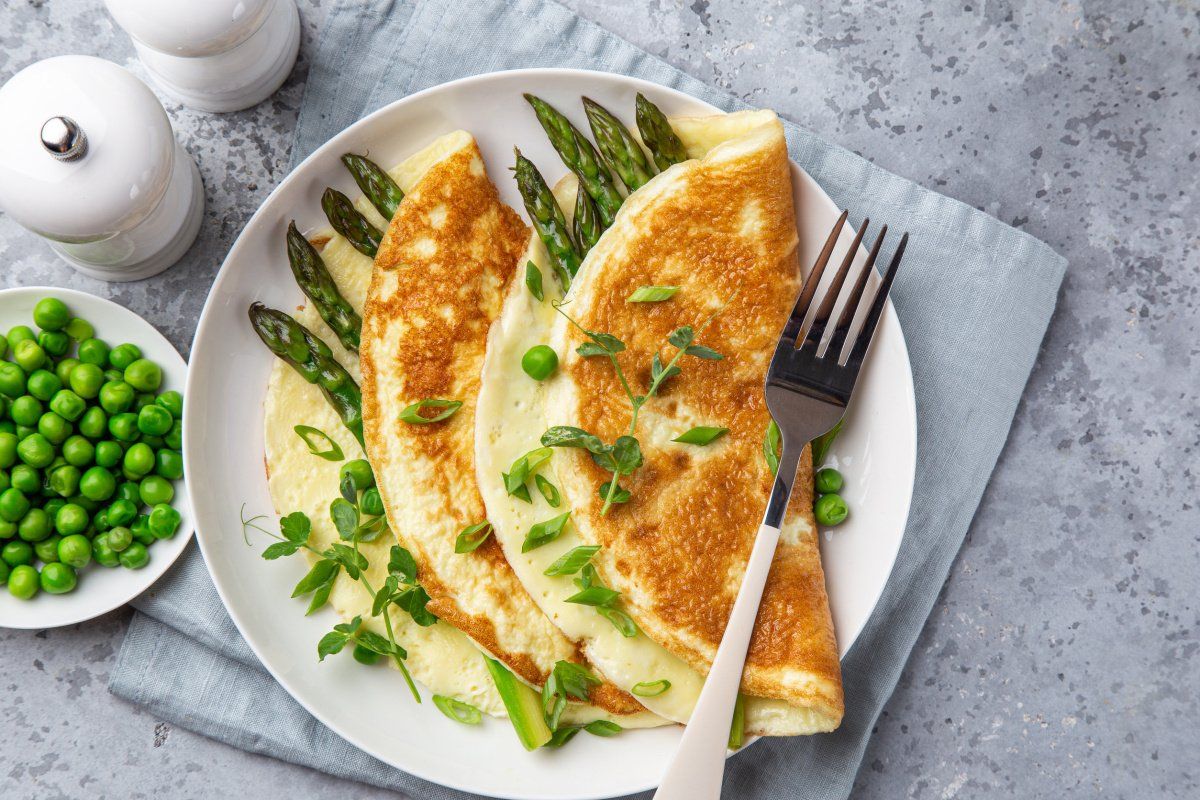 Omelette dorée pliée aux asperges vertes, petits pois et pousses de pois fraîches.