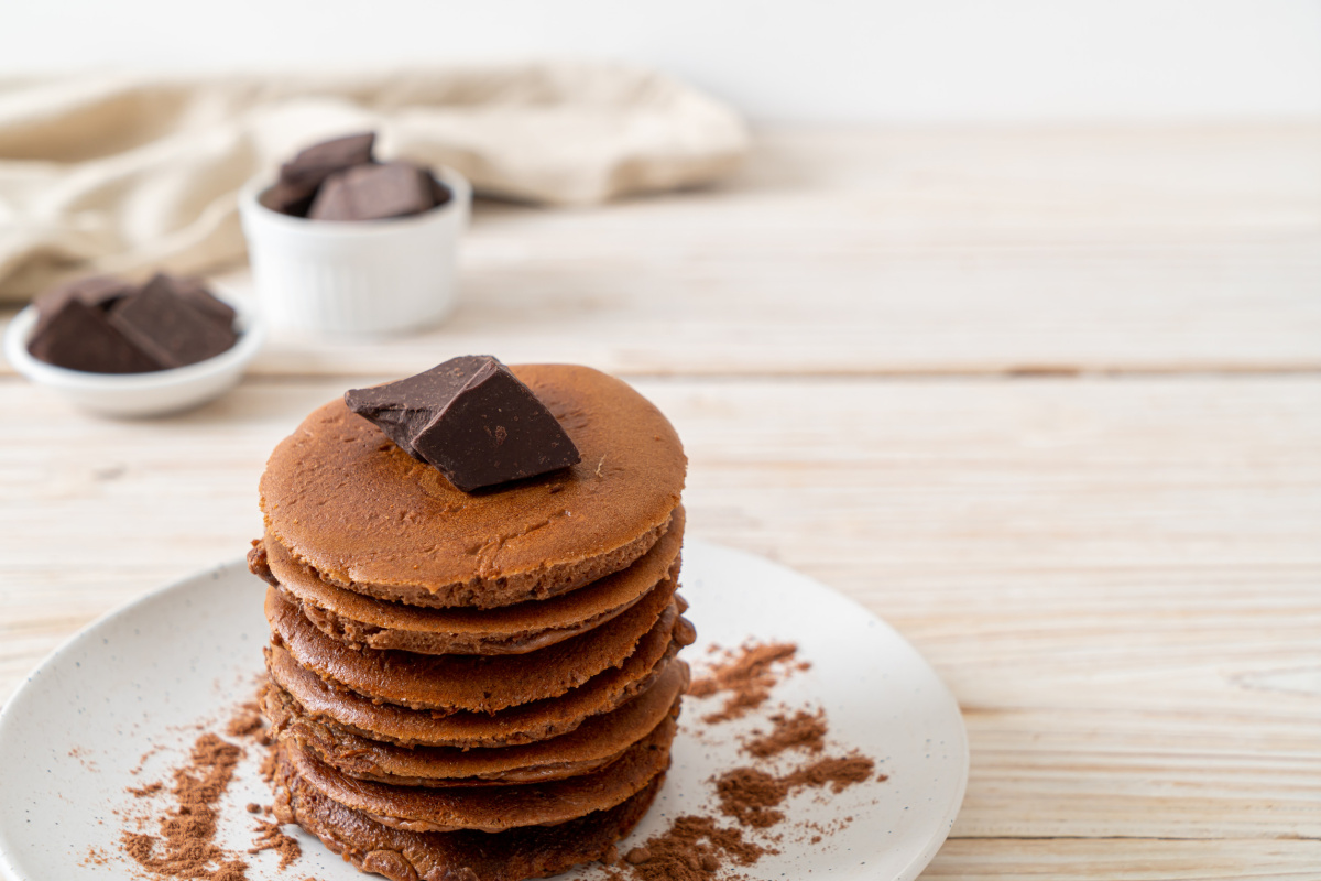 Pile de pancakes au chocolat d&eacute;cor&eacute;s de cacao et chocolat en morceaux.